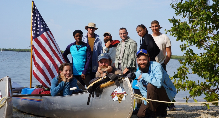 a group of veterans gathers around a canoe with an american flag.